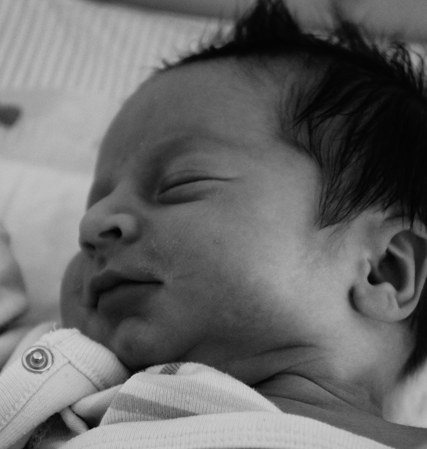"Schwarz-weiß Nahaufnahme eines schlafenden neugeborenen Babys in Seitenansicht, das friedlich und geborgen wirkt.