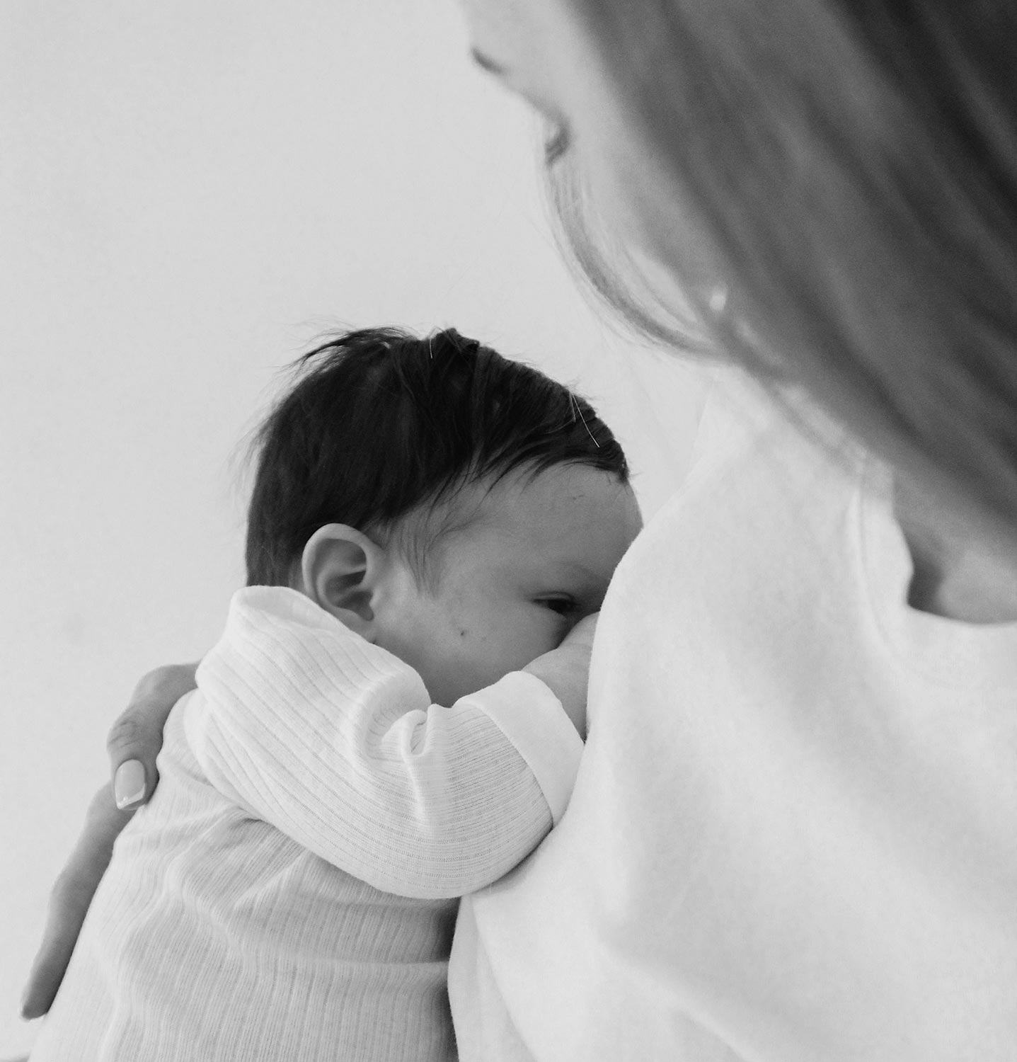 Schwarz-weiß Nahaufnahme einer Frau, die ein neugeborenes Baby behutsam an ihre Brust schmiegt und sicher in den Armen hält.
