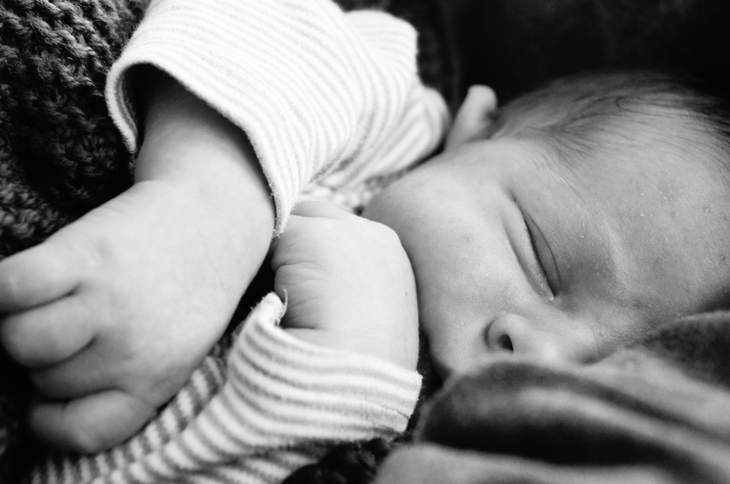 Schwarz-weiß Nahaufnahme eines wachen neugeborenen Babys mit großen, neugierigen Augen, das sanft zur Seite blickt.