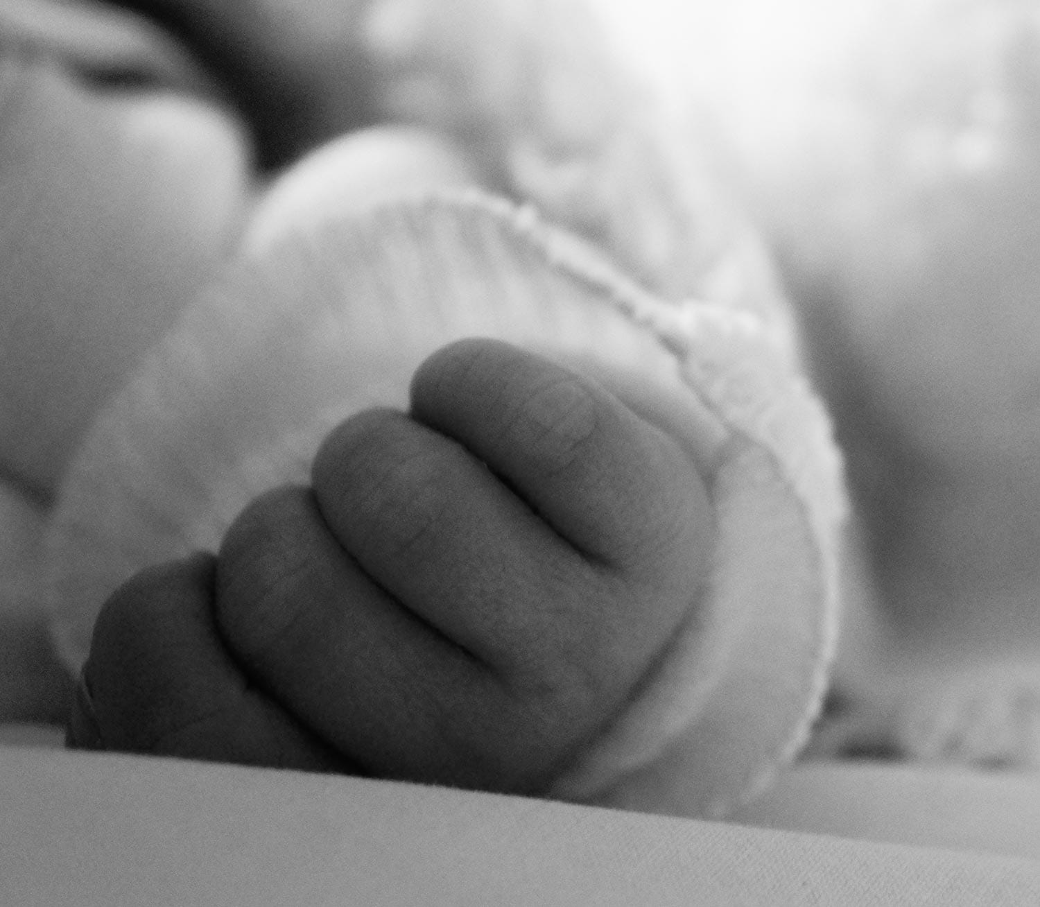 Schwarz-weiß Nahaufnahme der winzigen, geballten Faust eines neugeborenen Babys in einem weichen Strickärmel.